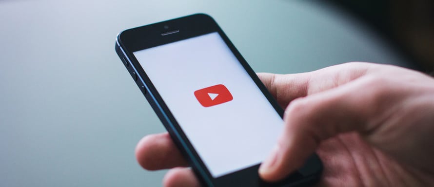 Une personne tenant un smartphone avec un logo youtube dessus.