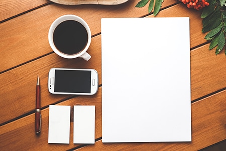 Une feuille de papier blanche et une tasse de café sur une table en bois.