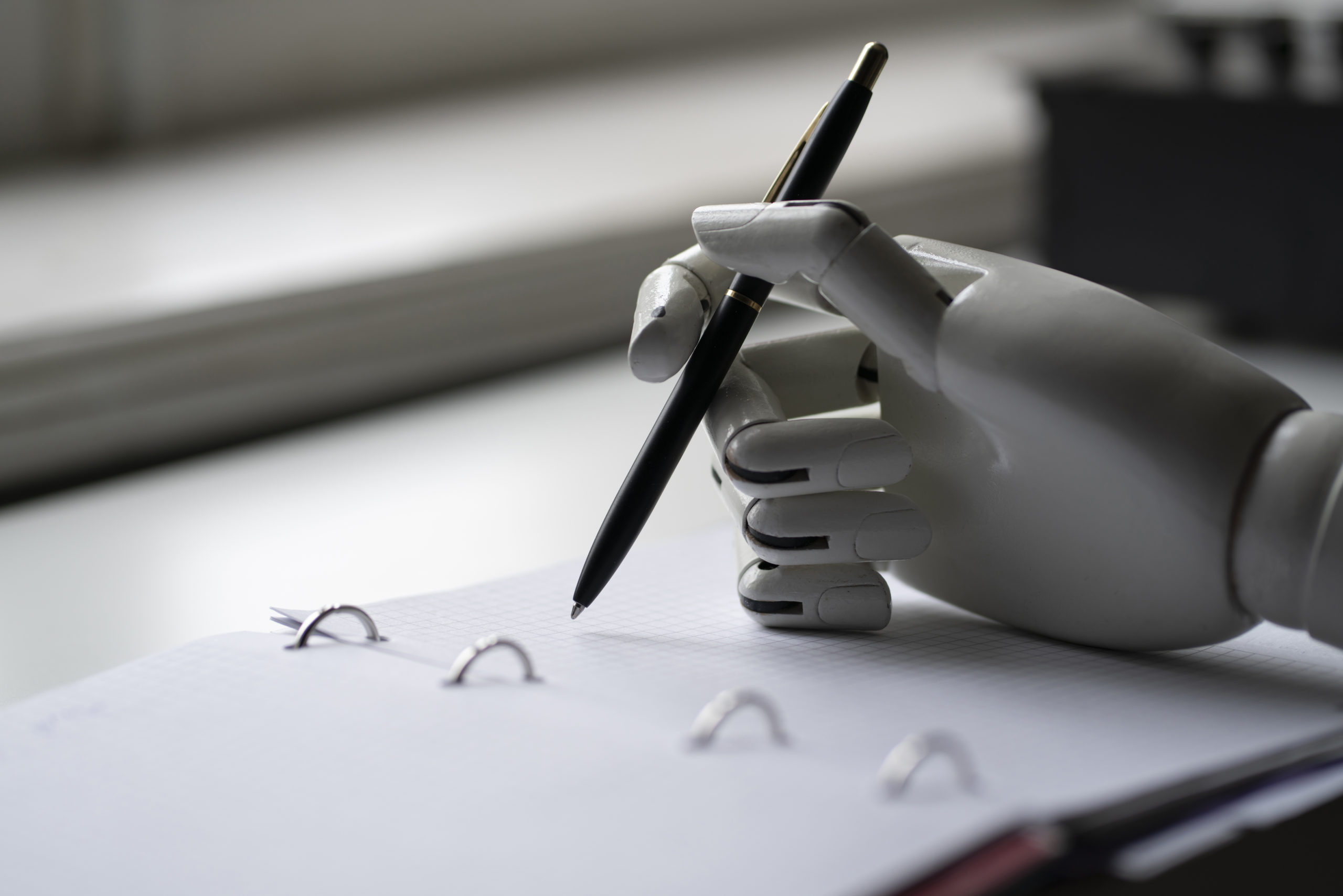 Une main de robot écrivant sur un bloc-notes avec un stylo.